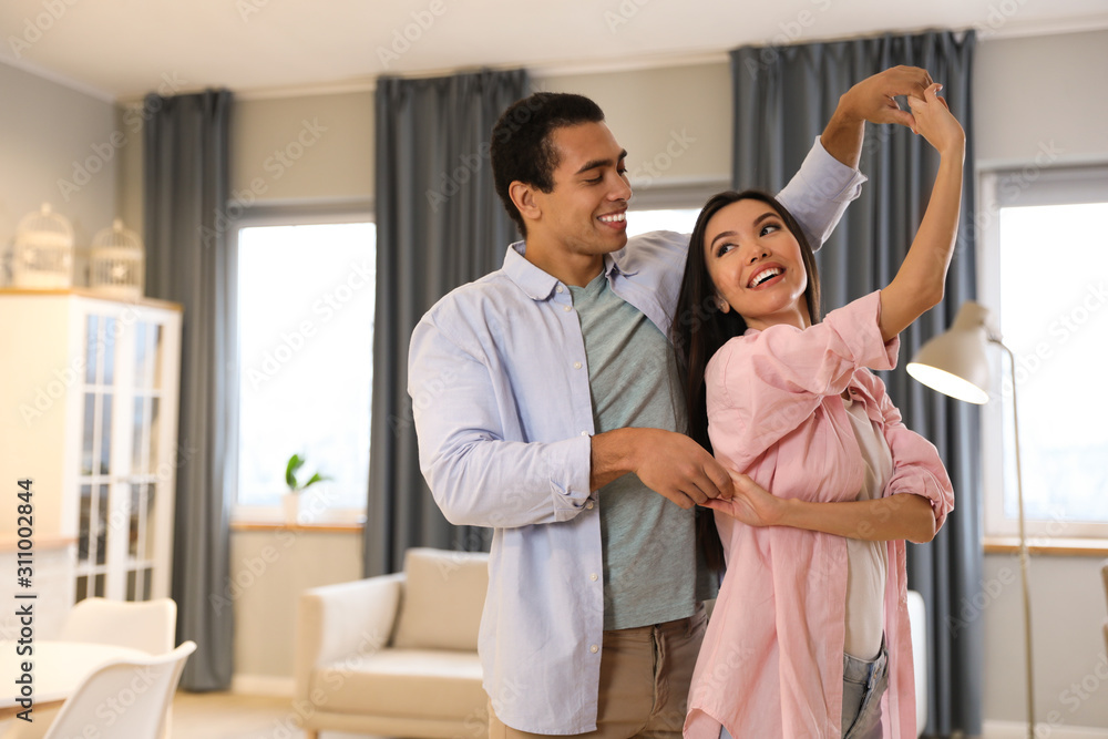 Fototapeta premium Lovely young interracial couple dancing at home. Space for text