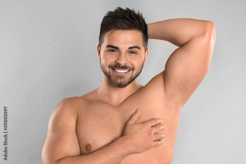 Young man showing hairless armpit after epilation procedure on grey background