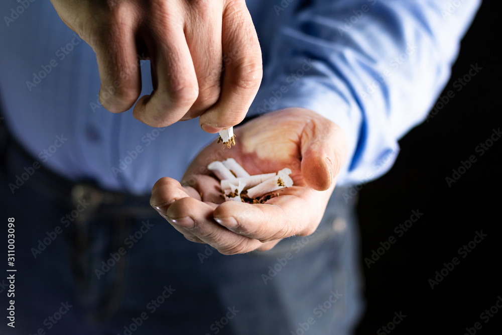 man in a blue shirt, dark background. he has a broken cigarette in his hand. he spills tobacco