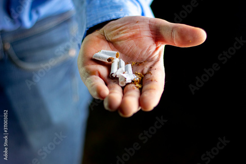 man in a blue shirt, dark background. he has a broken cigarette in his hand. he spills tobacco