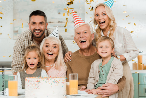 Wall Mural happy family looking at camera while sitting near birthday cake under falling co
