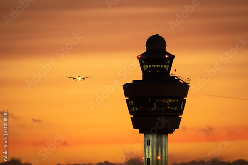 Amsterdam Schiphol International Airport control tower with a plane landing in the background during sunset. photo