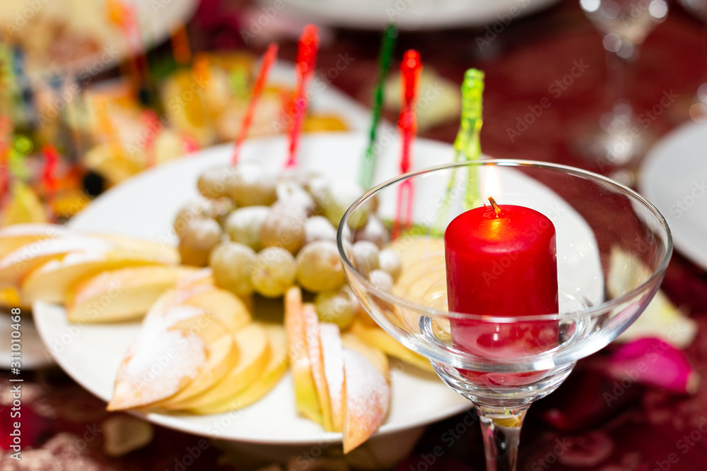 A candle in a glass goblet next to a plate food appetizers on red tablecloth in a restaurant.