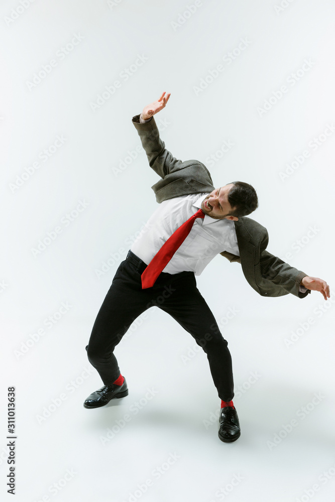 Young caucasian man moving flexible on white studio background. Male model in office attire bending over, avoiding something, catched in motion and action. Looks angry, scared, fighting. Emotions.