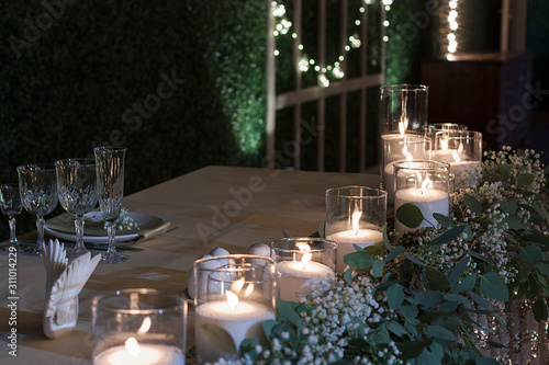 Glass vases with burning candles stand on the festive table on the wedding day. Table set