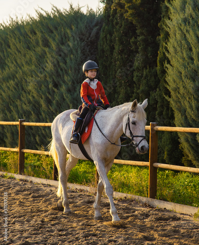 Bild auf Leinwand Kid riding white horse during horseback lessons.