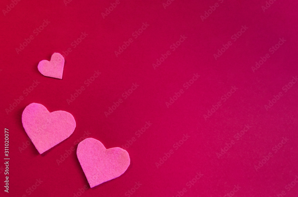 Pink felt hearts on a red background. St. Valentine's Day and romance concept. Top view, flat lay. Copy space.
