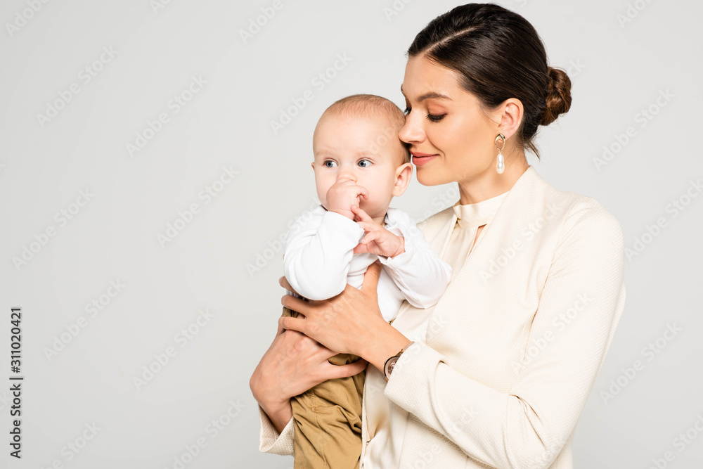 attractive positive businesswoman holding baby boy on hands, isolated on grey attractive positive businesswoman holding baby boy on hands, isolated on grey
