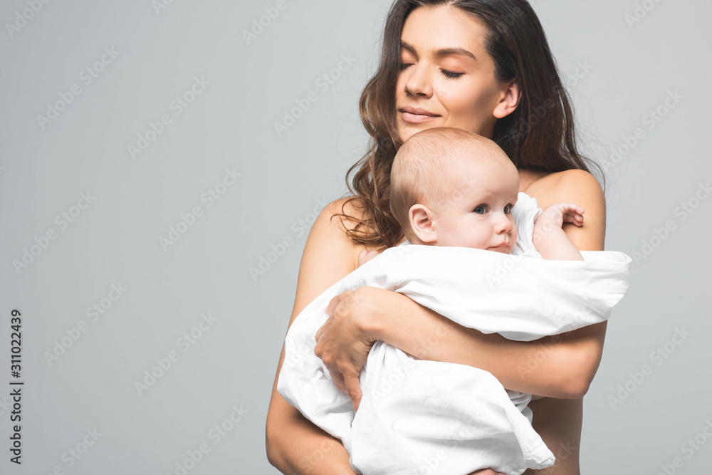portrait of happy naked mother hugging baby boy, isolated on grey