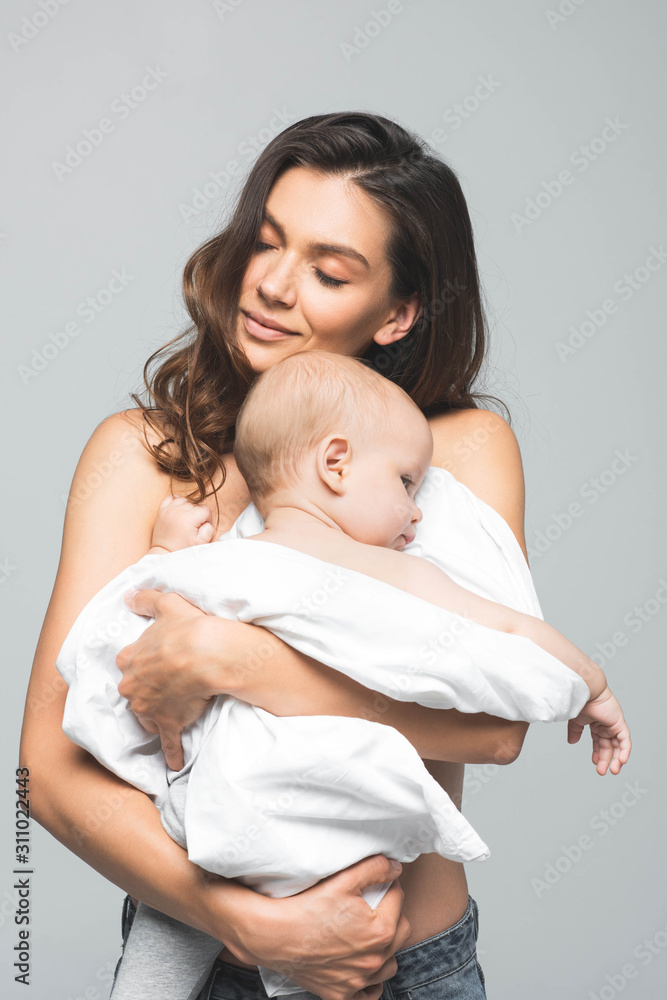portrait of happy naked mother with closed eyes hugging baby, isolated on grey