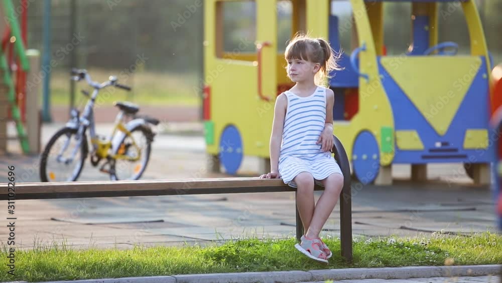 Cute child girl having fun sitting on a bench on summer playground in kindergarten yard. Cute child girl having fun sitting on a bench on summer playground in kindergarten yard.