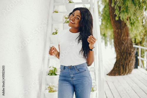 Cute black girl near white wall. Lady in a white t-shirt and blue jeans. Woman with watch