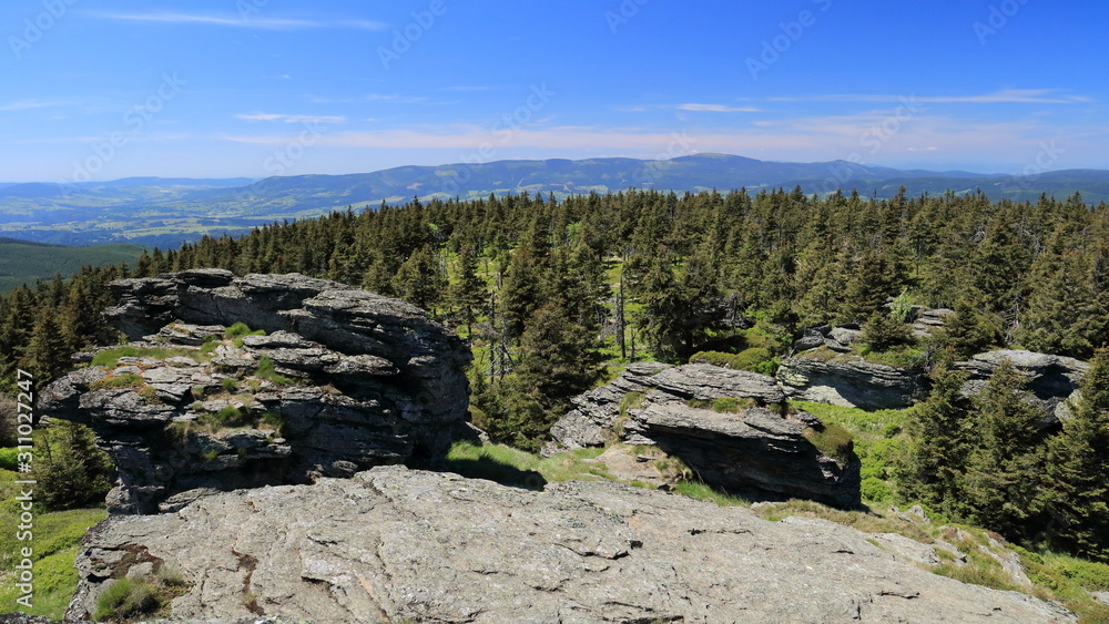 Forested mountain ridge with huge stones in the foreground.
