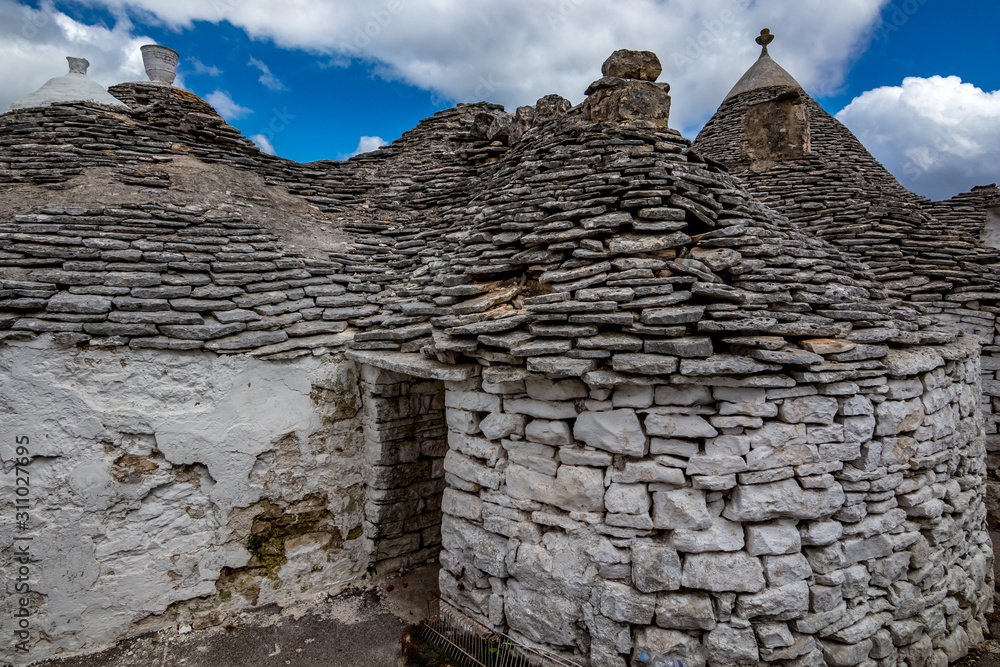 Roofs and entrance of truli, typical whitewashed cylindrical houses in Alberobello, Puglia, Italy with amazing blue sky with clouds, street view Roofs and entrance of truli, typical whitewashed cylindrical houses in Alberobello, Puglia, Italy with amazing blue sky with clouds, street view