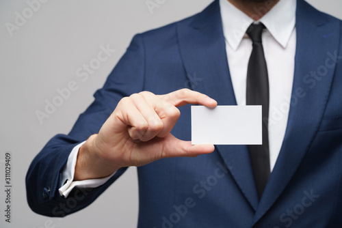 studio photo of young handsome businessman wearing suit holding business card