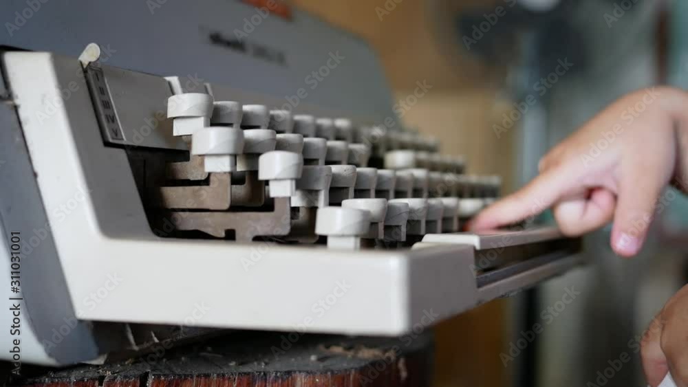The side view of cute child girl typing on a vintage typewriter in cafe. The side view of cute child girl typing on a vintage typewriter in cafe.