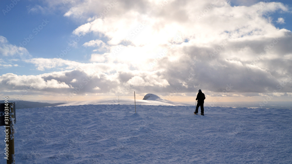 A snowshoe hiker walking on snow, on top of a snowy volcanic mountain
