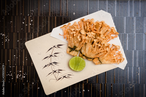 deep fried golden brown crispy Japanese enokitake needle shape mushroom with lime on black backgroundstock photo photo