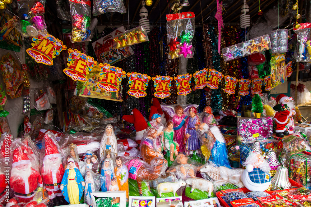Fototapeta premium Jarmark noworoczny, Wielka wyprzedaż choinek i lalki Mikołaja. Sprzedaż sztucznych jodeł i świątecznych dekoracji w namiotach. Wesołych Świąt i Szczęśliwego Nowego Roku 2020.