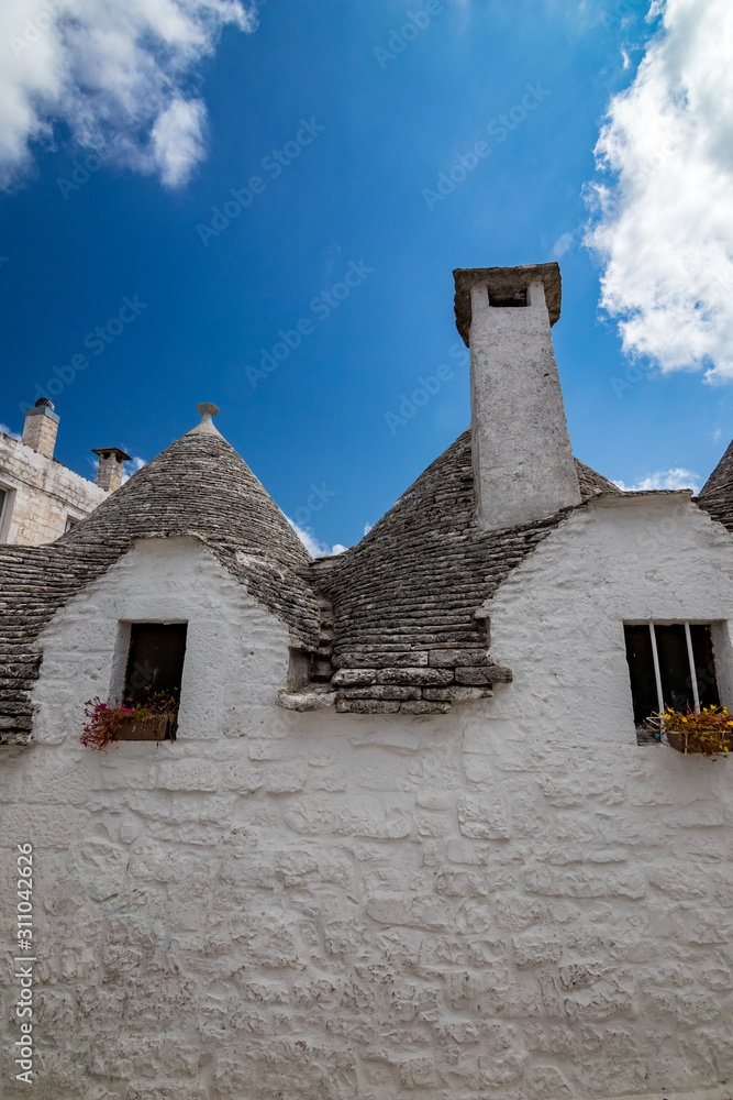 Roofs of truli, typical whitewashed cylindrical houses in Alberobello, Puglia, Italy with amazing blue sky with clouds, street view, small windows and chimney