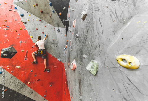 Sportsman climber moving up on steep rock, climbing on artificial wall indoors. Extreme sports and bouldering concept
