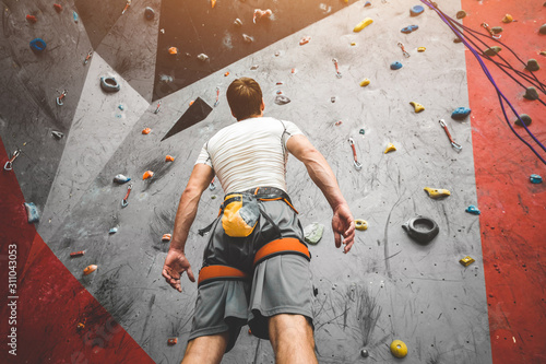 Sportsman climber is looking on steep rock, climbing on artificial wall indoors. Extreme sports and bouldering concept