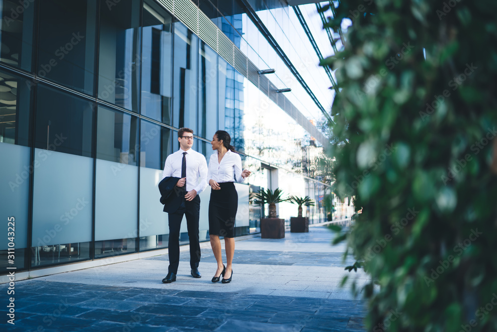 Elegant talking coworkers on street Contemporary diverse man and woman in classy outfits chatting friendly while strolling down empty street with modern building on background Elegant talking coworkers on street Contemporary diverse man and woman in classy outfits chatting friendly while strolling down empty street with modern building on background