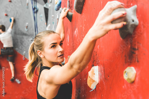 Sportswoman climber moving up on steep rock  climbing on artificial wall indoors. Extreme sports and bouldering concept