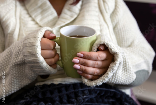 Female hands in a white sweater hold a mug with a hot drink. Hot tea warms not only the body, but also the soul.