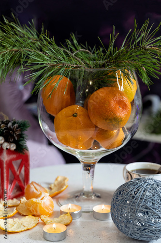 A vase with tangerines, pine branches, candles and handmade Christmas toys stand on a white table. The concept of preparation for the holiday. New Year card. Selective focus.