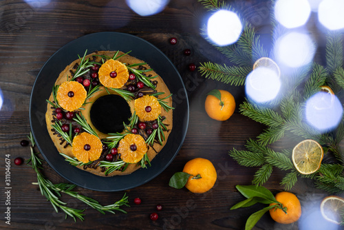 Valokuva Tangerine ring cake decorated with sliced mandarines, cranberries and rosemary on wooden background