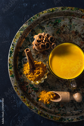 Golden turmeric milk on the dark background with spices cinnamon and ingredients
