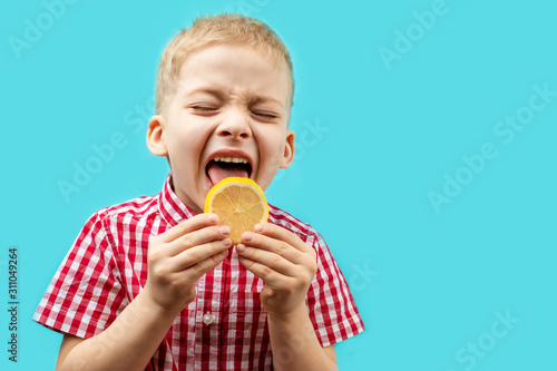 child tastes the lemon. vitamin C is very useful for children. the boy in the red shirt on a blue background