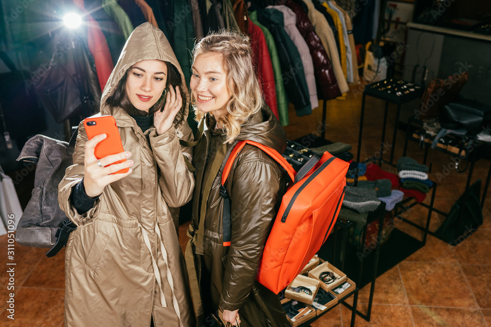 Obraz premium Three women taking a selfie while shopping in a clothing store. They are happy and smiling at camera. Shopping concept, also related to social media addiction.