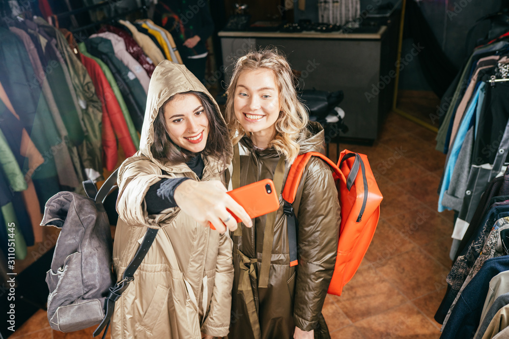Fototapeta premium Two women taking a selfie while shopping in a clothing store. They are happy and smiling at camera.