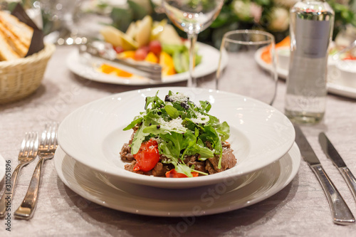 Fresh salad with tomatoes, beef, lettuce and arugula on plates in restaurant
