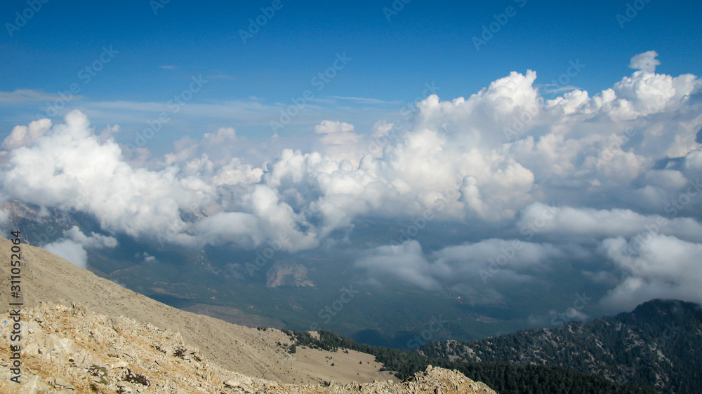 view from the top of the mountain to the mountains covered with white clouds against the blue sky on a sunny day