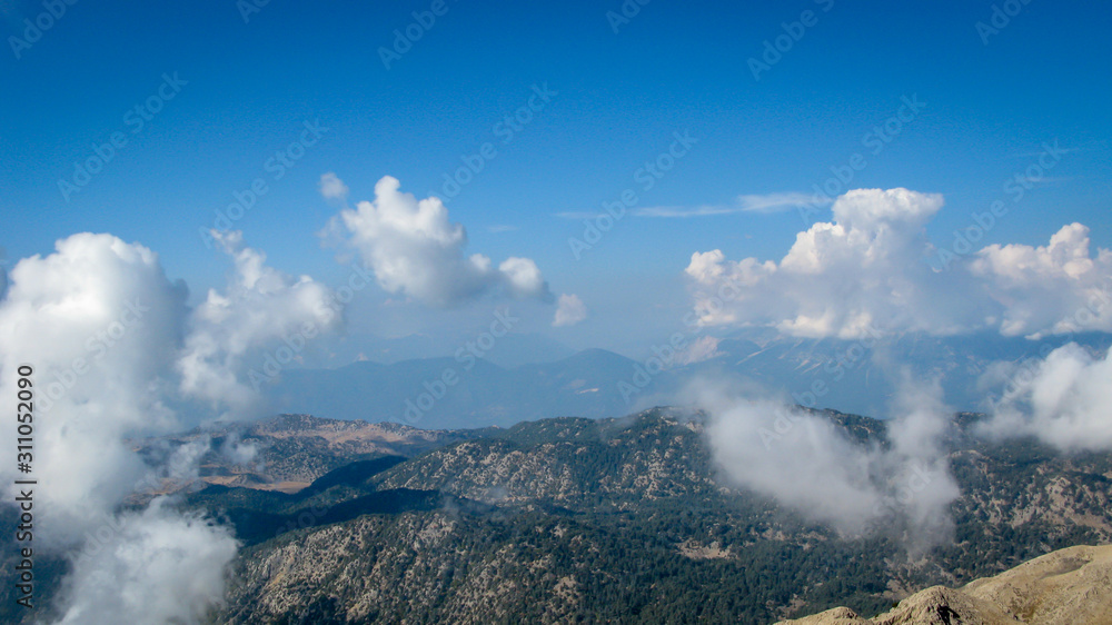 Obraz premium view from the top of the mountain to the mountains covered with white clouds against the blue sky on a sunny day