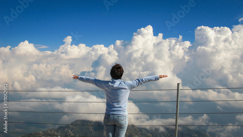 woman stands on top of a mountain near abyss on a background of blue sky and white clouds on a sunny day