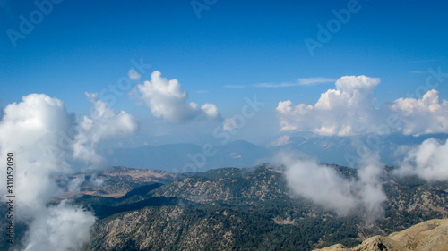 view from the top of the mountain to the mountains covered with white clouds against the blue sky on a sunny day
