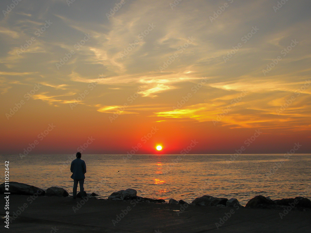 man on the seashore looks at dawn, blue sky and white clouds