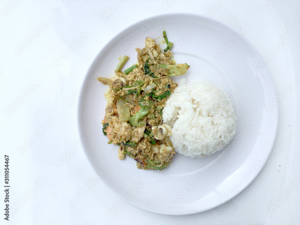 Stir fry mixed-seafood with with yellow curry powderin thai style with fried egg and rice in in white plate on white background. Stir fry mixed-seafood with with yellow curry powderin thai style with fried egg and rice in in white plate on white background.