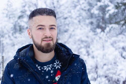 Young handsome man in snowy forest looking at camera in casual clothes