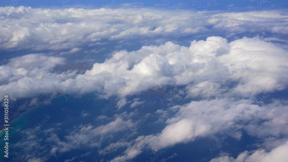 View from airplane window - flying over clouds, sea and coast below View from airplane window - flying over clouds, sea and coast below
