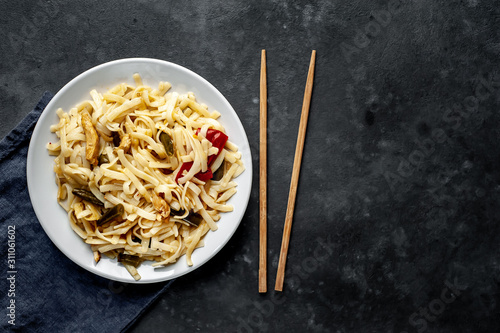 Asian food udon noodles with chicken and vegetables on a white plate on a stone background with copy space for your text