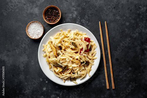 Asian food udon noodles with chicken and vegetables on a white plate on a stone background