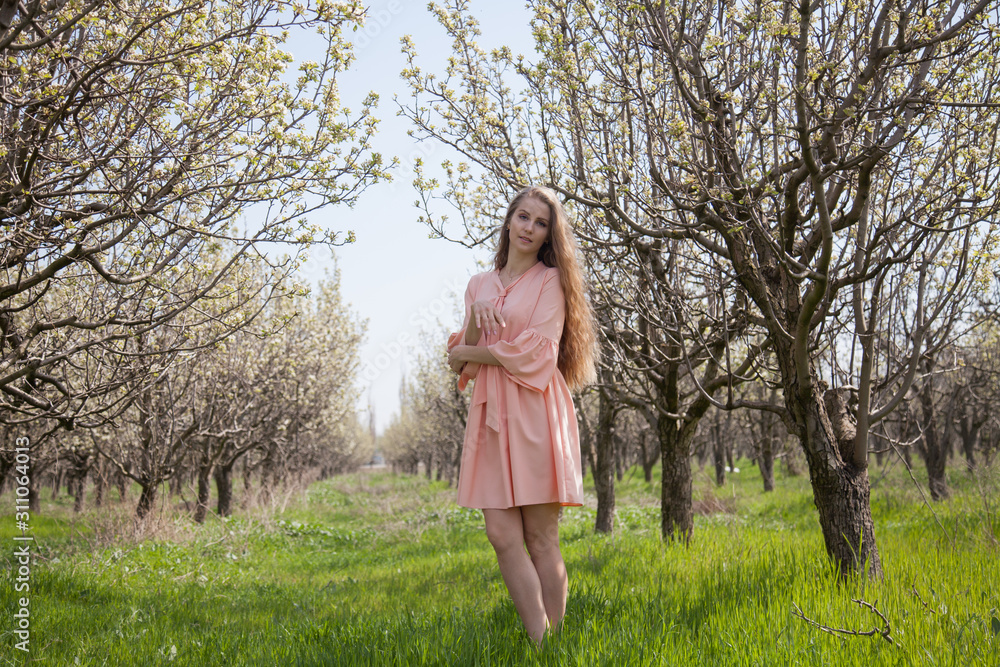 Beautiful blonde woman in pink dress in green flowering garden in spring