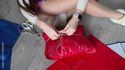 brunette girl is wrapping a gift for the new year, against the background of a snowman, wrapping paper on the floor