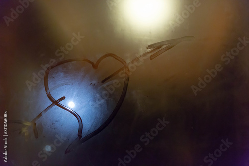 The symbol of the heart of the Cupid pierced by an arrow painted on the misted glass with a blue and yellow spot of light in the background.