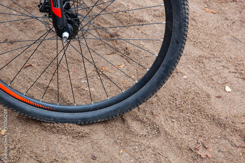 Part of the Bicycle wheel on the black rim stands on sandy soil.